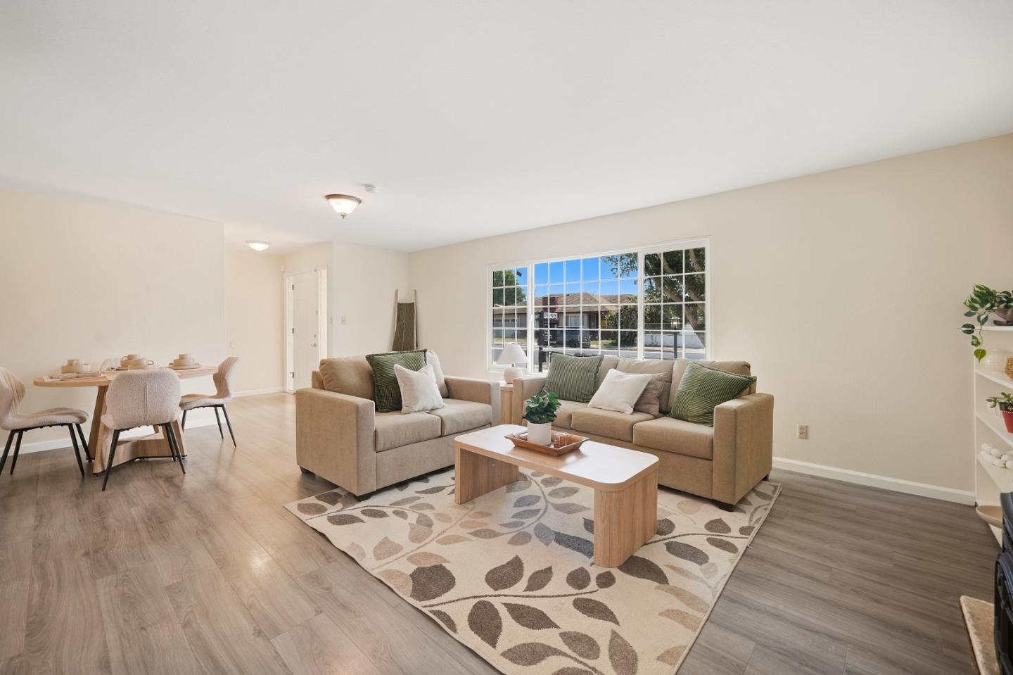 Staged living room with beige sofas, green pillows, a patterned rug, and an adjoining dining area.