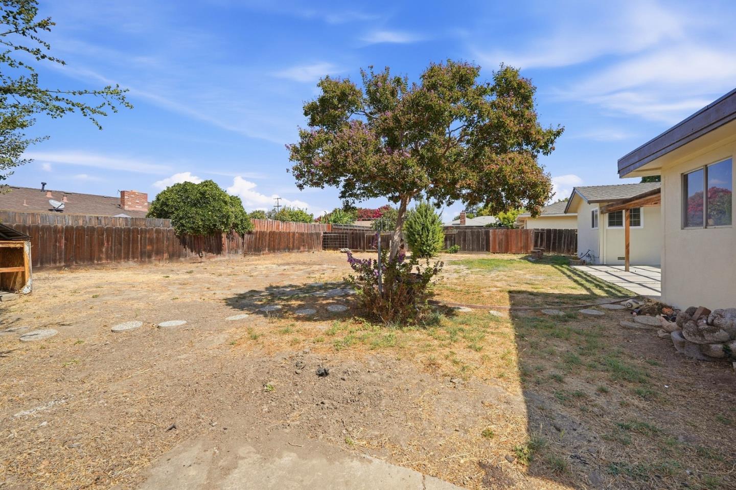 Backyard with a mature tree, dry lawn, wooden fencing, and a covered patio.