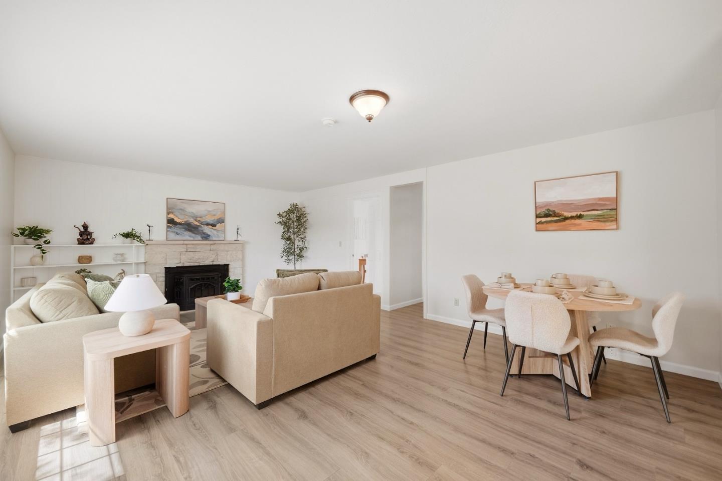 Staged living and dining room with a fireplace, neutral seating, and light wood-look floors.