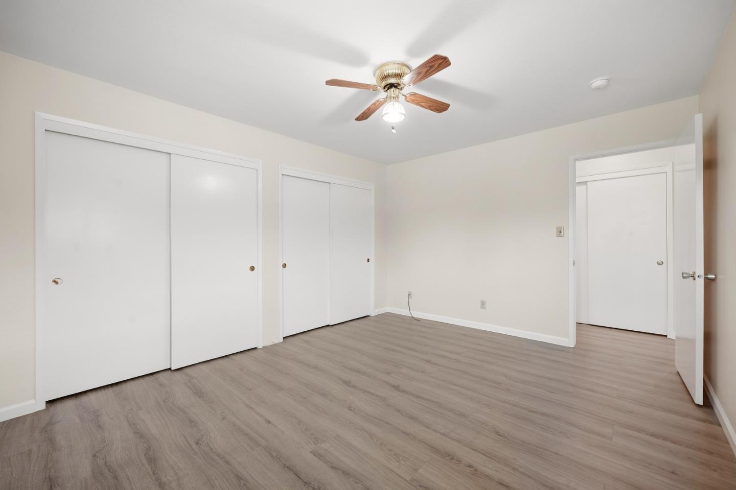 Empty bedroom with gray wood-look floors, sliding closets, and a ceiling fan.