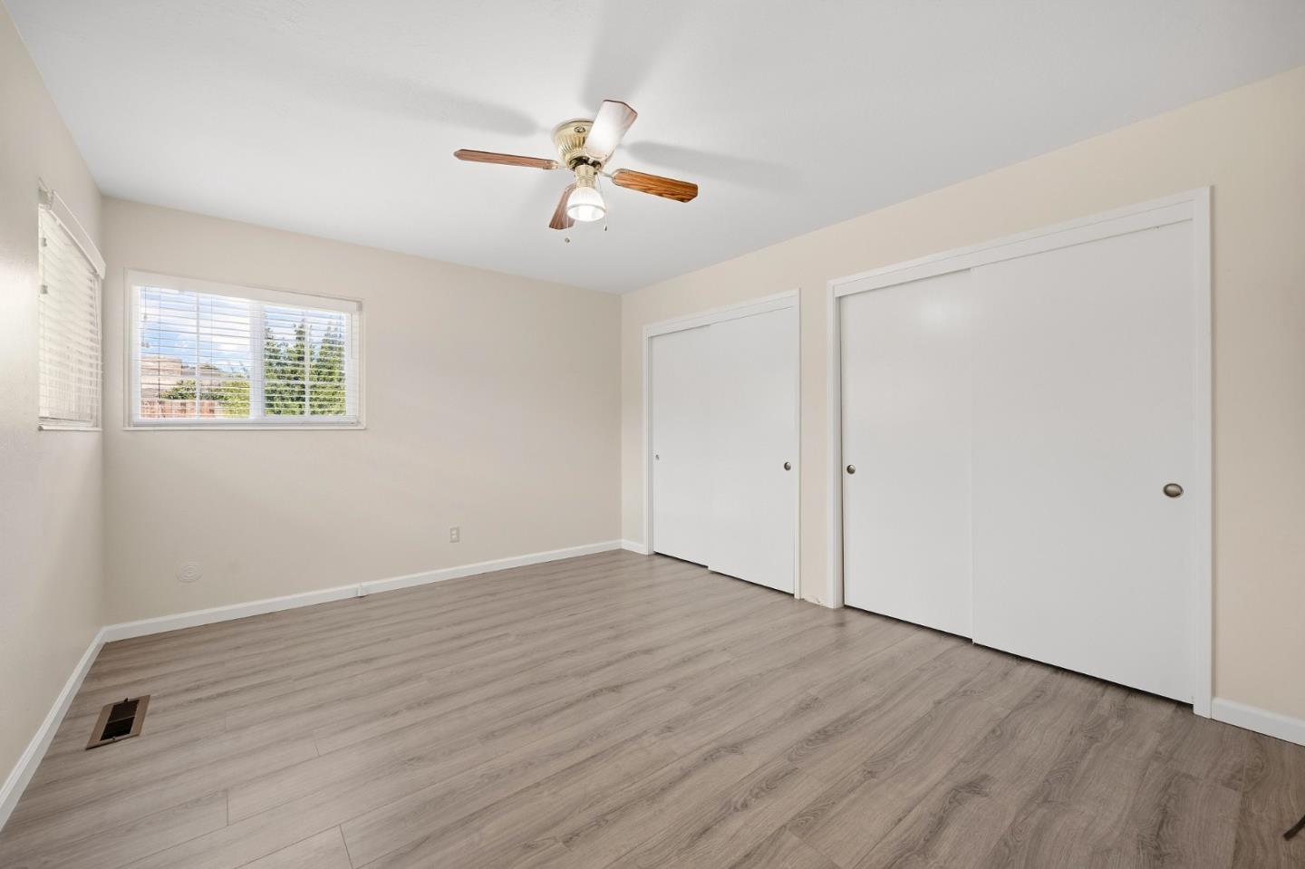 Empty bedroom with light wood-look flooring, two windows, white closet doors, and a ceiling fan.