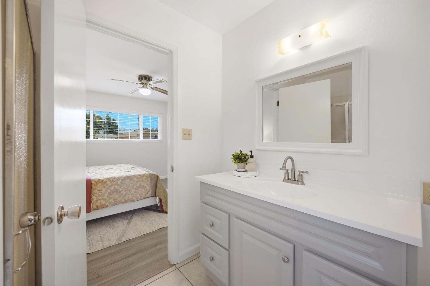 Bathroom vanity with a large mirror and doorway to a bedroom with a wide window.