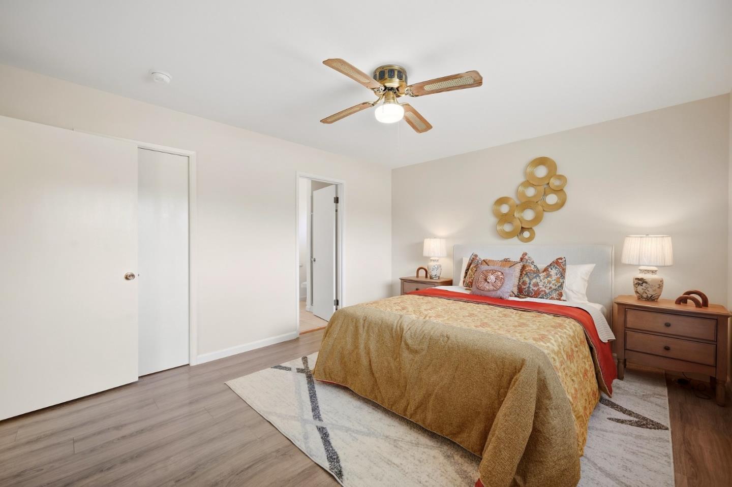 Furnished bedroom with gold and red bedding, wooden nightstands, and a ceiling fan.