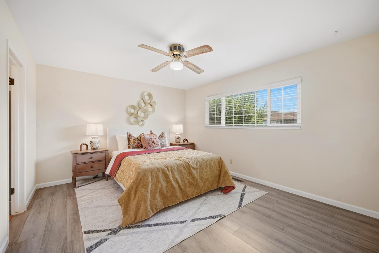 Staged bedroom with a gold-covered bed, matching nightstands, and a wide window with blinds.