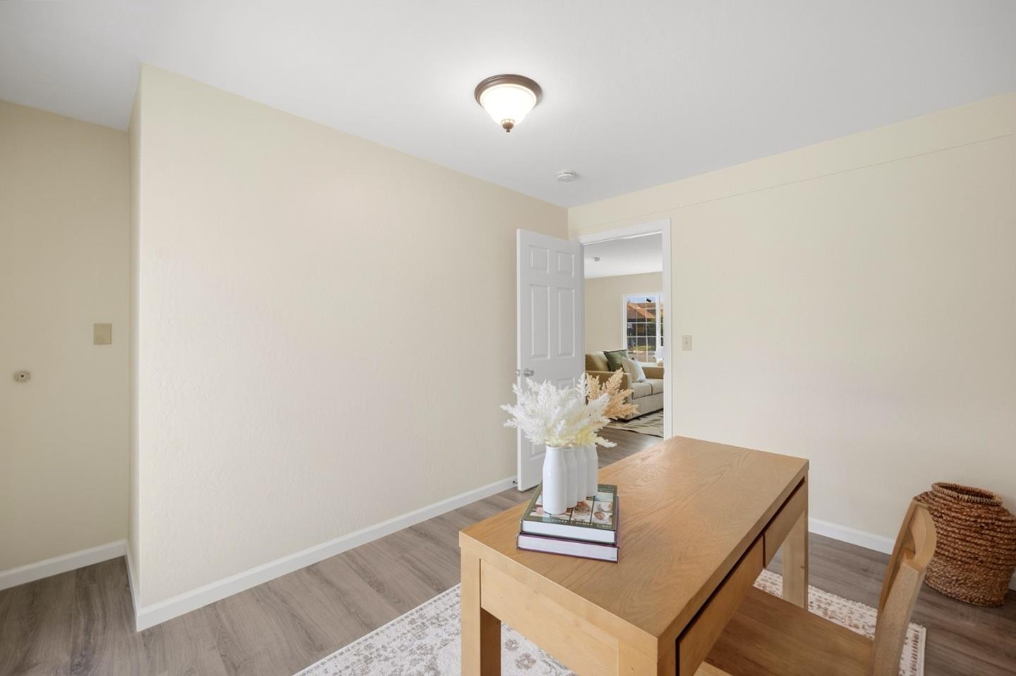 Staged home office with a light wood desk and an open doorway to the living room.