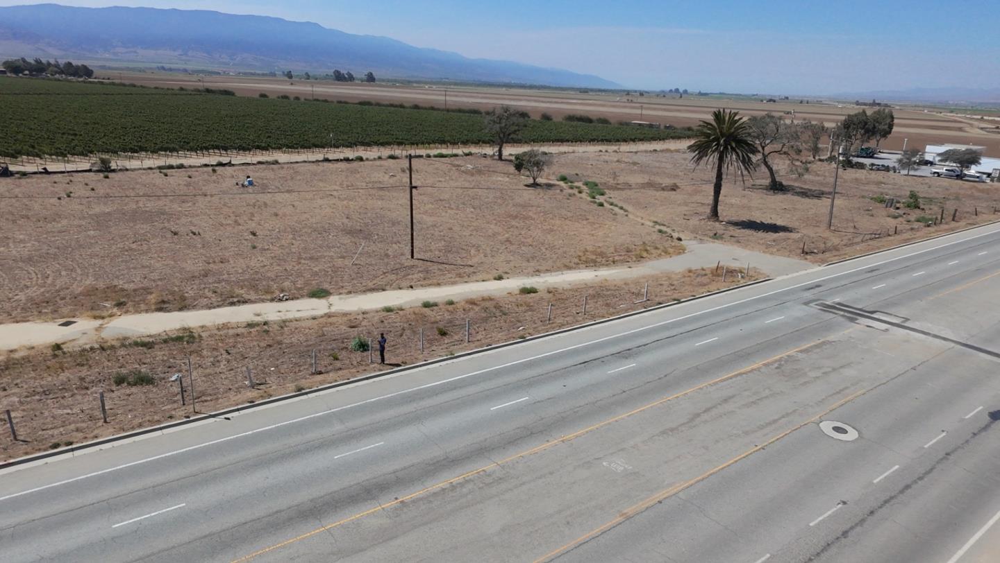 Vacant roadside parcel beside a highway, with farmland and mountains in the distance.