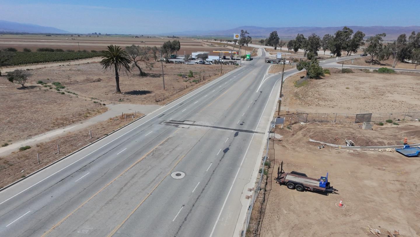 Aerial view of a dry roadside parcel beside a highway, with a trailer and agricultural fields nearby.