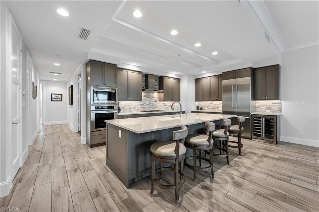 Modern kitchen with a large white island, four bar stools, dark cabinets, and stainless steel appliances.