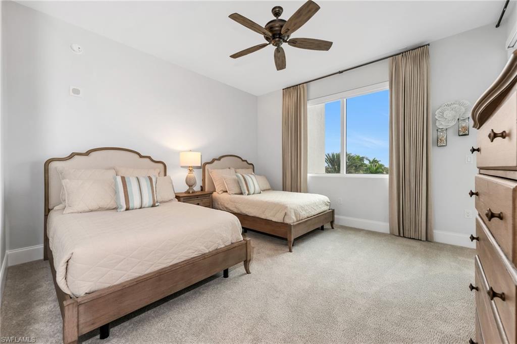 Bedroom with two wooden beds, pale bedding, and a window overlooking palm trees.