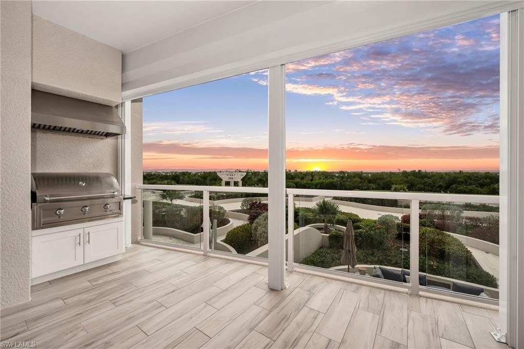 Covered condo balcony with a built-in grill overlooking landscaped grounds at sunset.