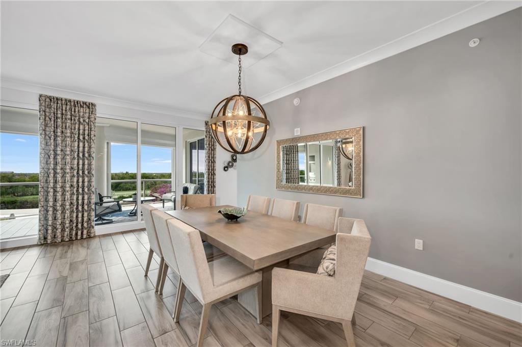 Dining room with a long wood table and upholstered chairs beside sliding doors to a balcony.