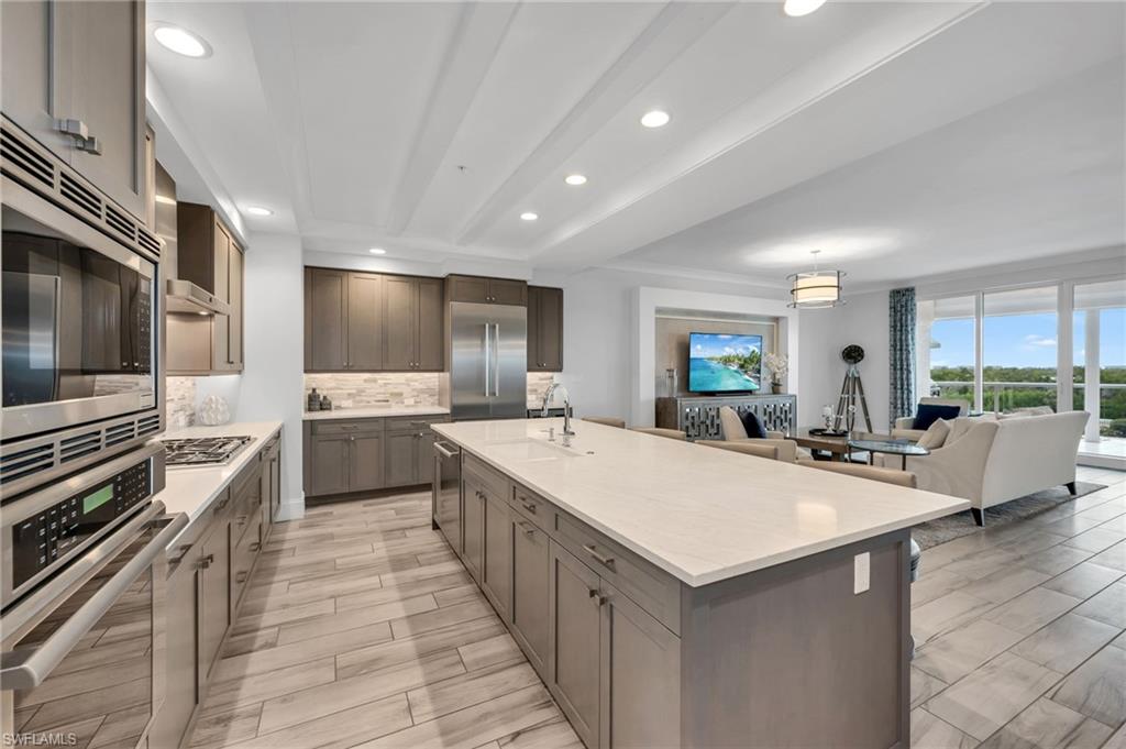 Open kitchen with a large white island, gray cabinets, stainless steel appliances, and adjoining living area.