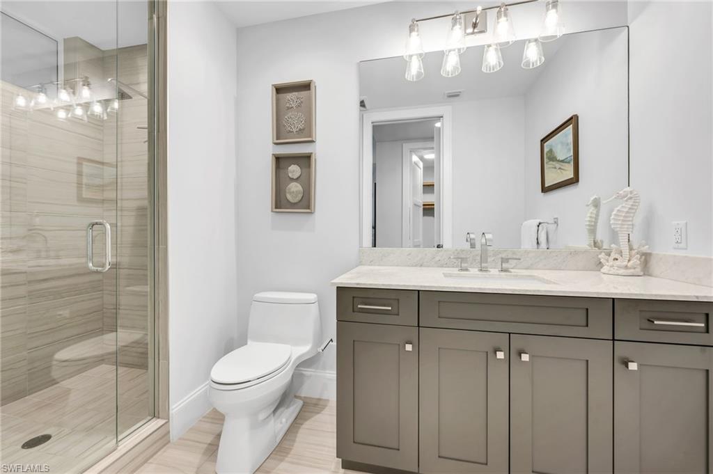 Bathroom with a glass-enclosed tiled shower and gray vanity topped with light stone.