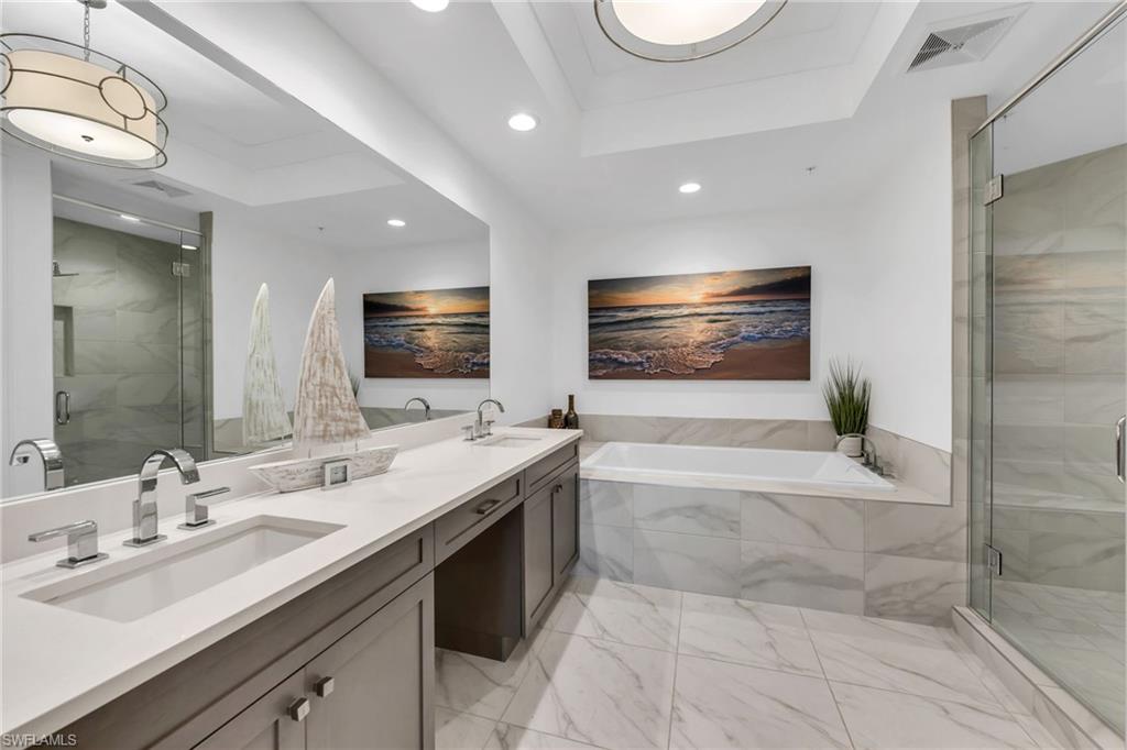 Bathroom with a double-sink vanity, soaking tub, and glass shower in marble-look tile.