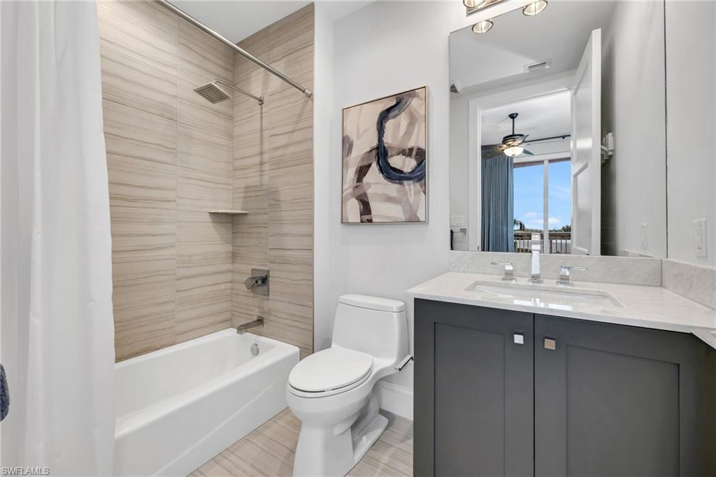Bathroom with a tiled tub and shower, gray vanity, large mirror, and abstract wall art.