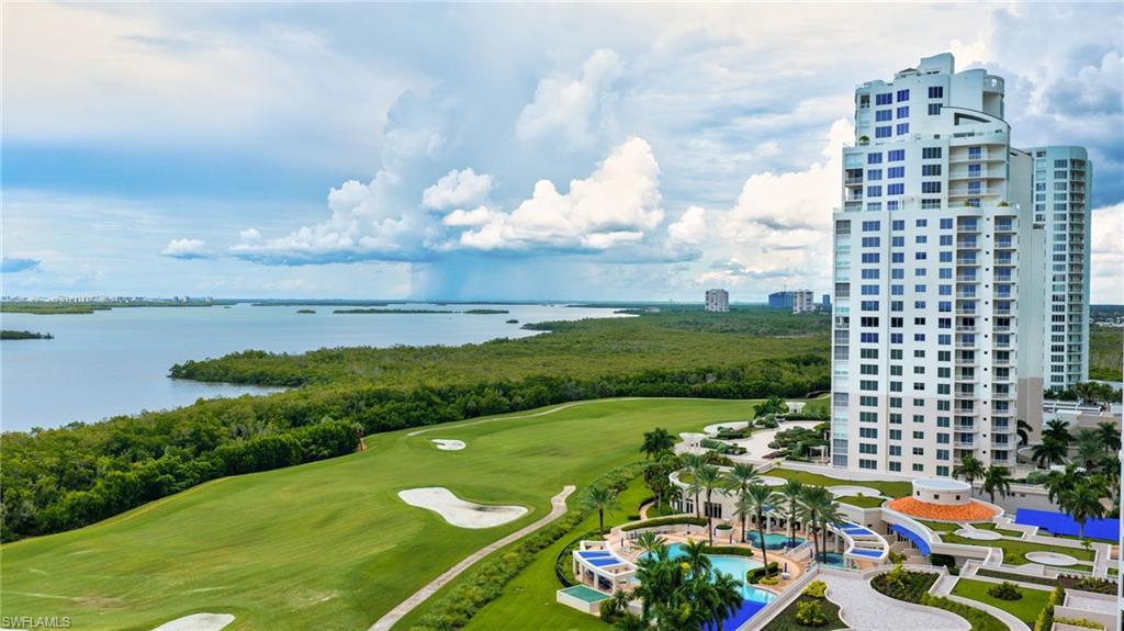 High-rise condominium overlooking a golf course and coastal water, with landscaped pool amenities below.