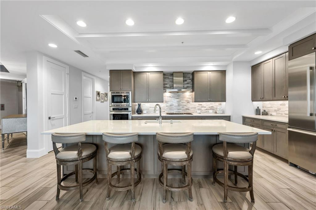 Kitchen with a large island and four bar stools, gray cabinets, and stainless steel appliances.