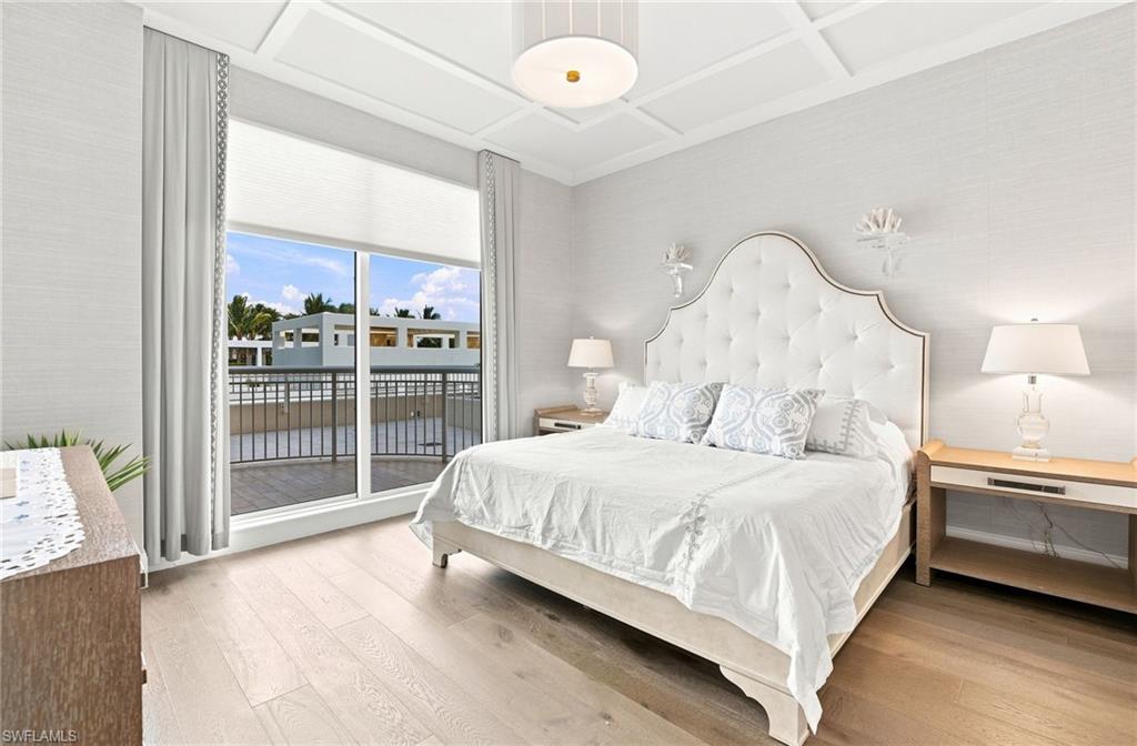 Bedroom with a white tufted bed, light wood floors, and sliding doors to a balcony.