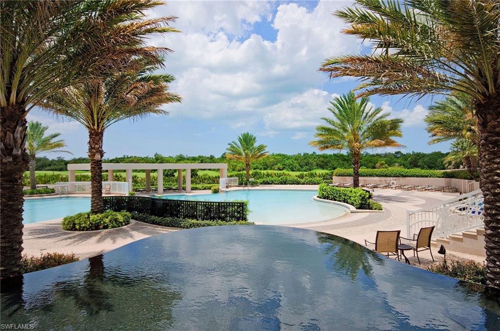 Outdoor pool framed by palm trees, with patio seating and a reflecting pool in the foreground.