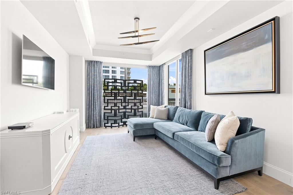 Living room with a blue-gray sectional, tray ceiling, and large windows overlooking nearby buildings.
