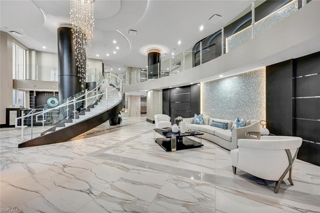 Condominium lobby with a sweeping staircase, marble-patterned floors, and modern seating.