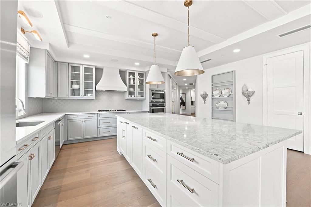 Renovated kitchen with a large stone island, gray cabinetry, stainless steel appliances, and wood floors.