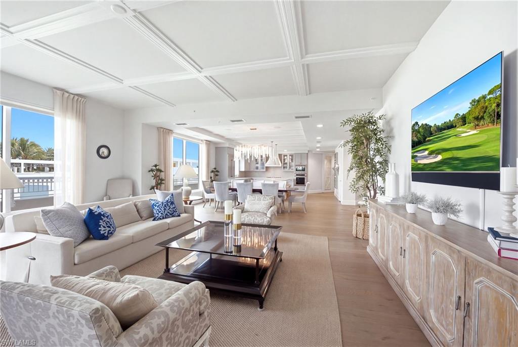 Open-plan living room with coffered ceiling, pale furnishings, and a television displaying a golf course.