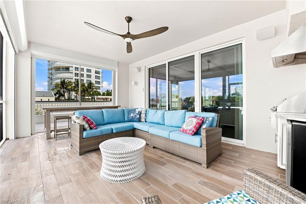 Covered condo lanai with blue sectional seating, a ceiling fan, and a view of a neighboring building.