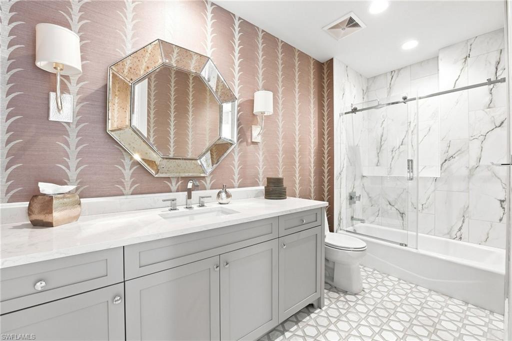 Bathroom with a gray vanity, octagonal mirror, and marble-look tub surround.