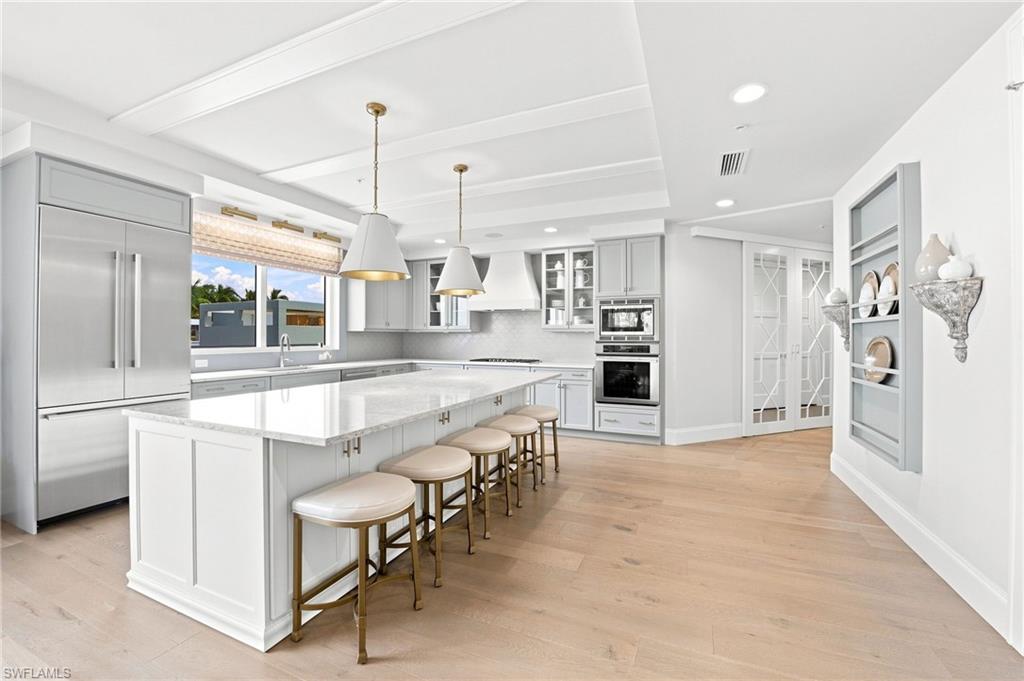 Bright kitchen with a large island, bar stools, stainless steel appliances, and light wood floors.