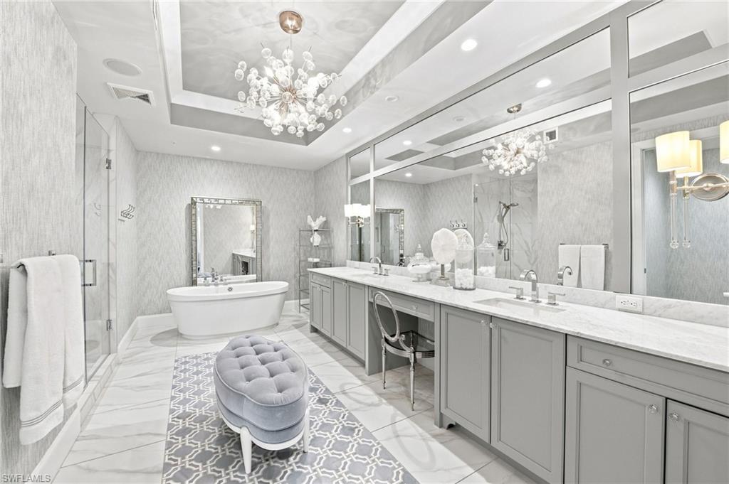 Bathroom with a freestanding soaking tub, mirrored double vanity, glass shower, and sculptural chandelier.