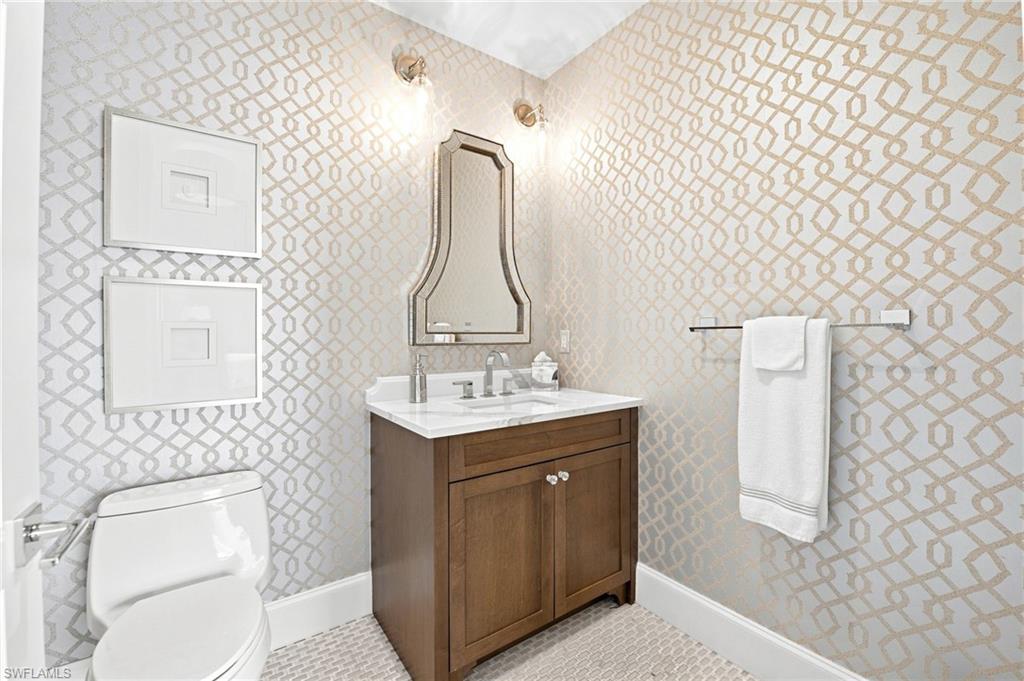 Bathroom with a wood vanity and white-and-gold geometric wallpaper.