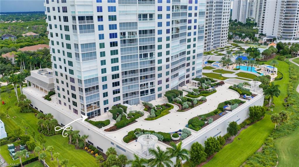Aerial view of a white condominium tower, landscaped grounds, and a pool.