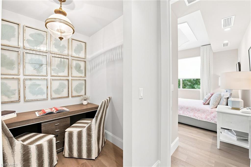 Home office with a framed-art wall beside a bedroom with a pink bedspread.