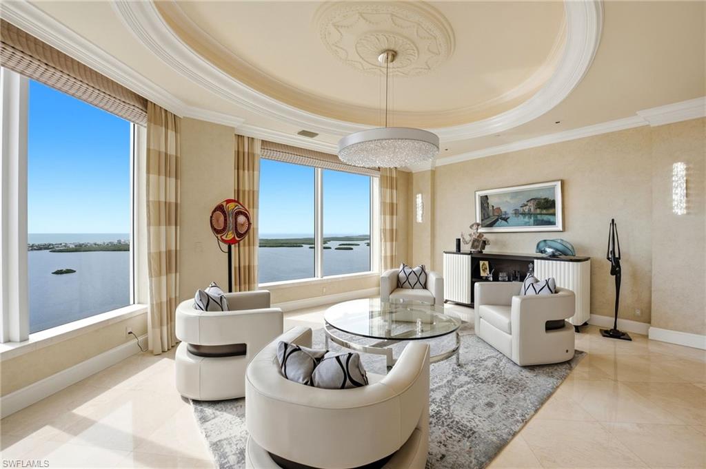 Furnished living room with curved white seating and expansive windows overlooking coastal water and islands.