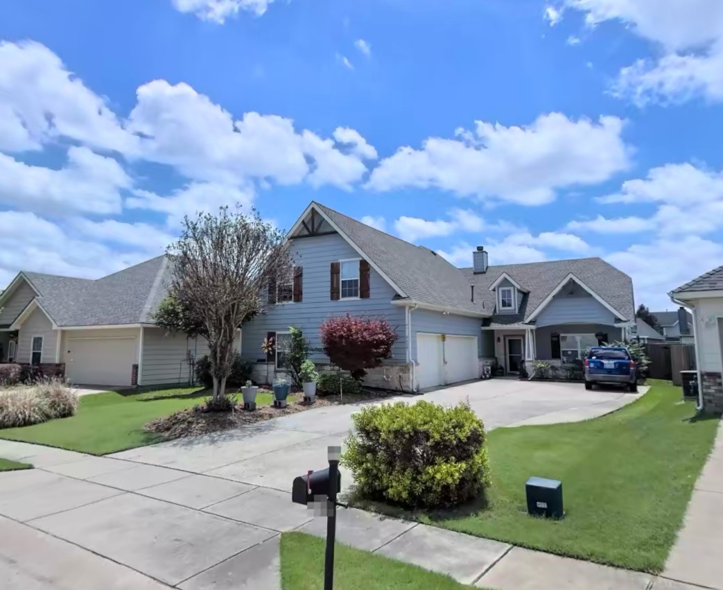 Blue-gray two-story home with attached garages, a wide driveway, and landscaped lawn.