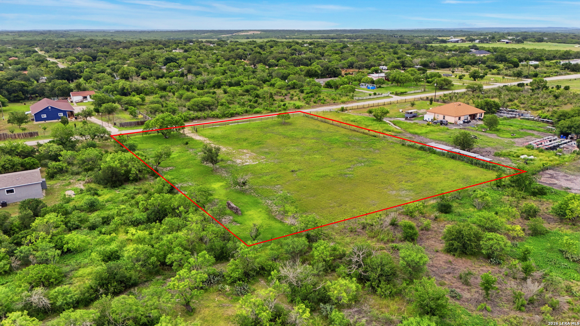 Aerial view of a grassy parcel outlined in red among trees and rural homes.