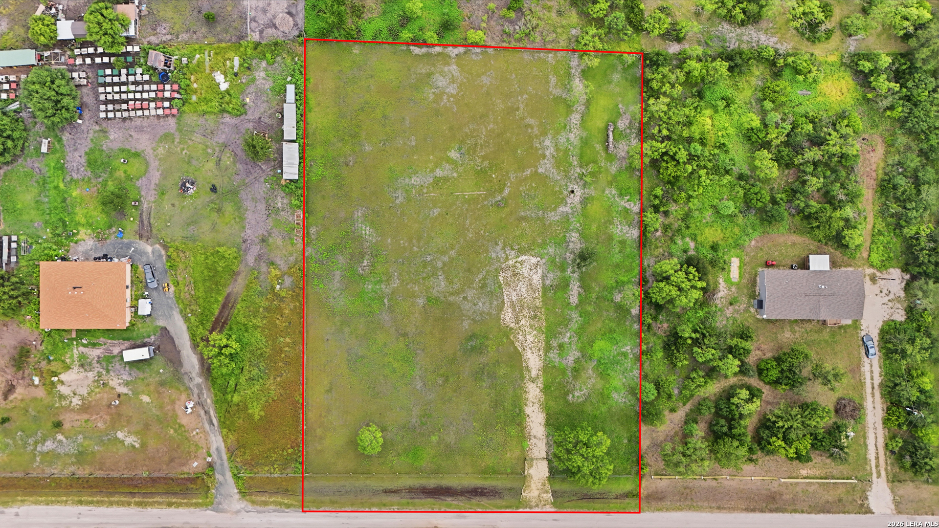 Aerial view of a vacant lot outlined in red, with a dirt track and neighboring homes nearby.