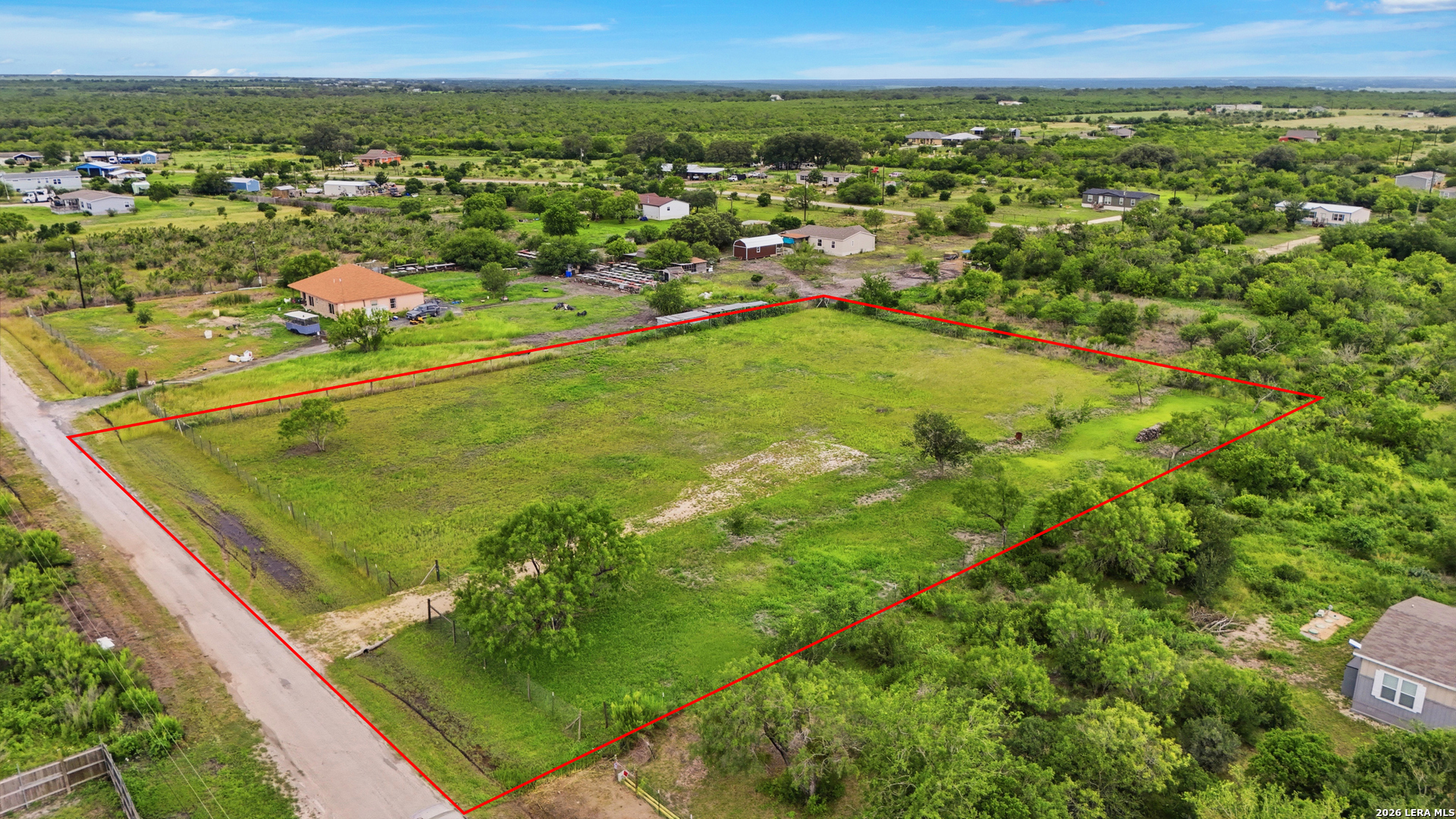 Aerial view of a fenced green parcel outlined in red beside a rural dirt road.