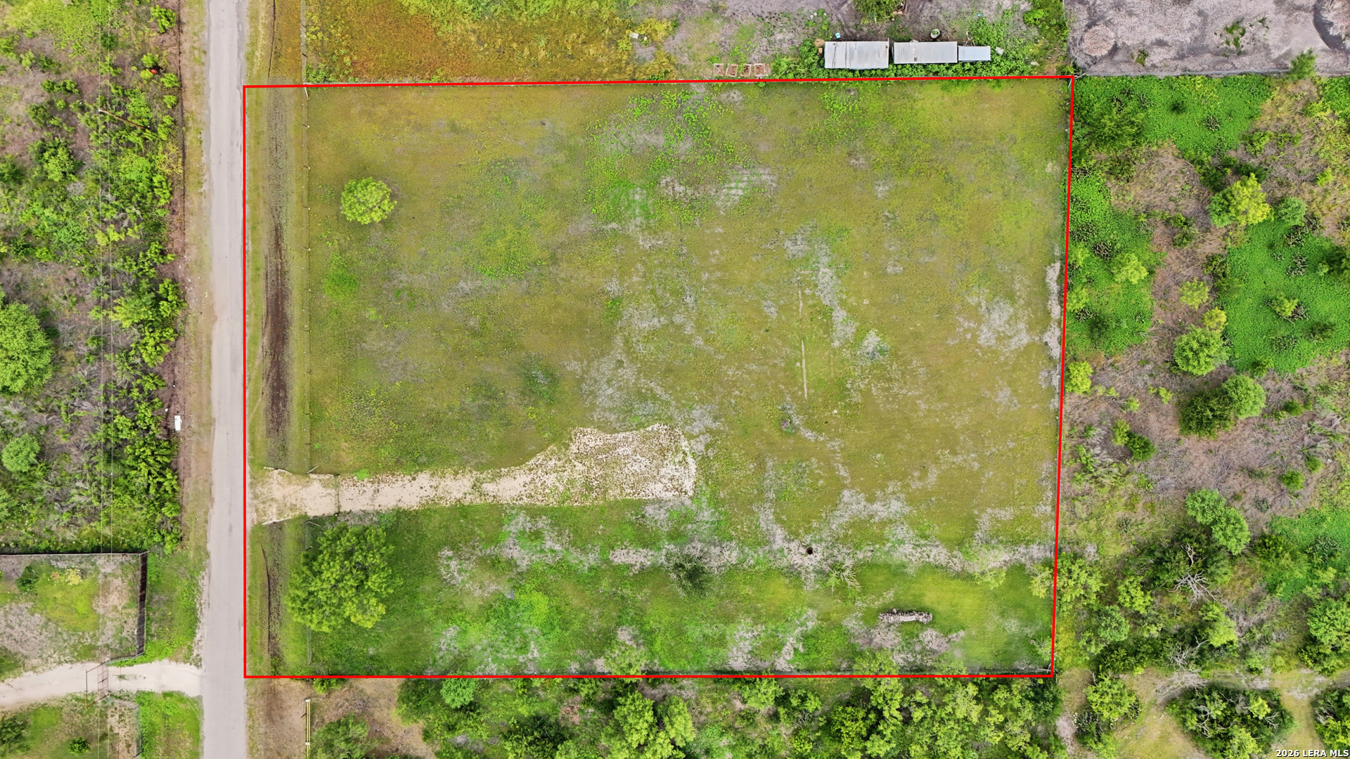 Aerial view of a grassy vacant parcel outlined in red beside a rural road.
