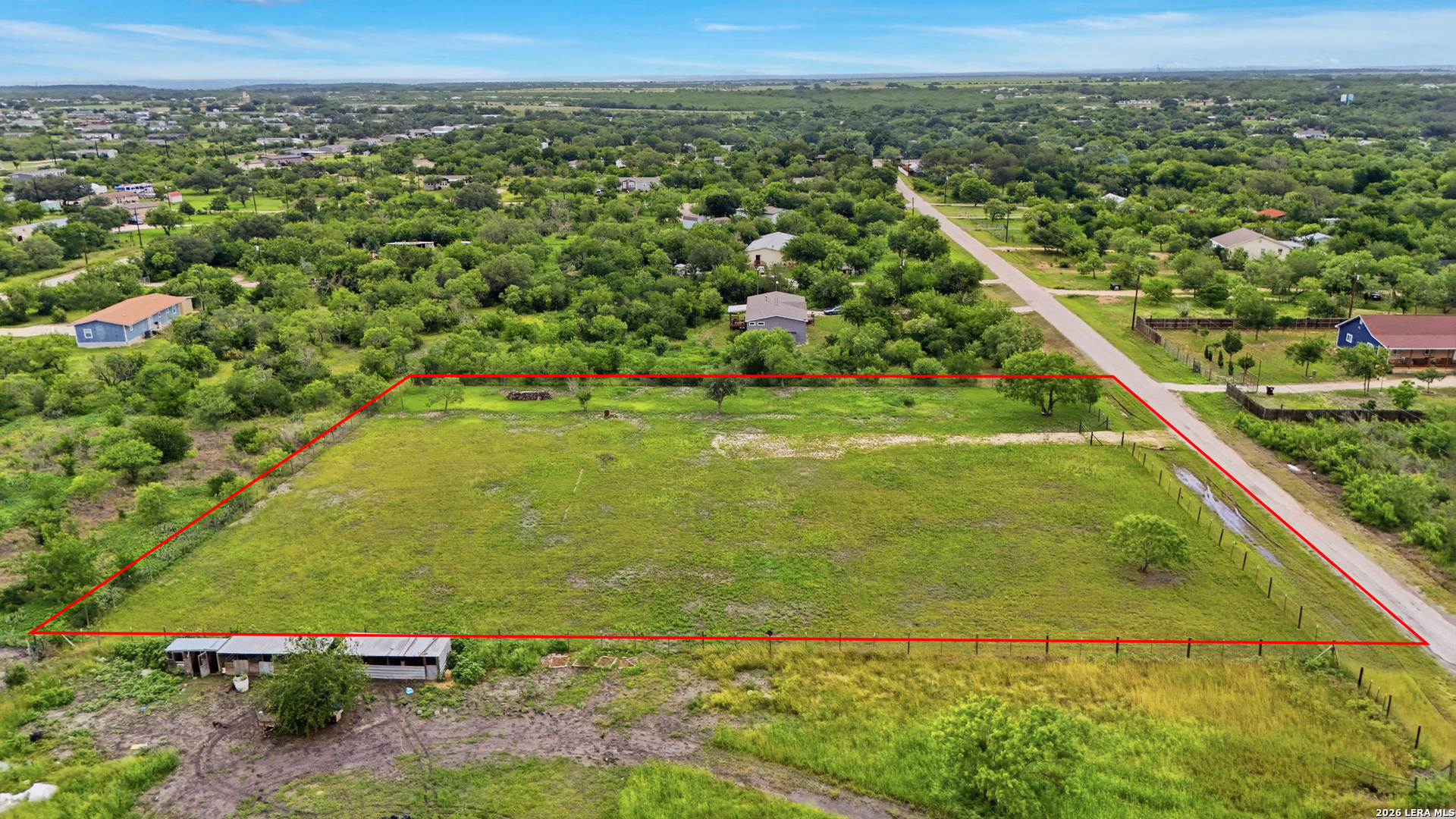 Aerial view of a grassy vacant parcel outlined in red beside a rural road.