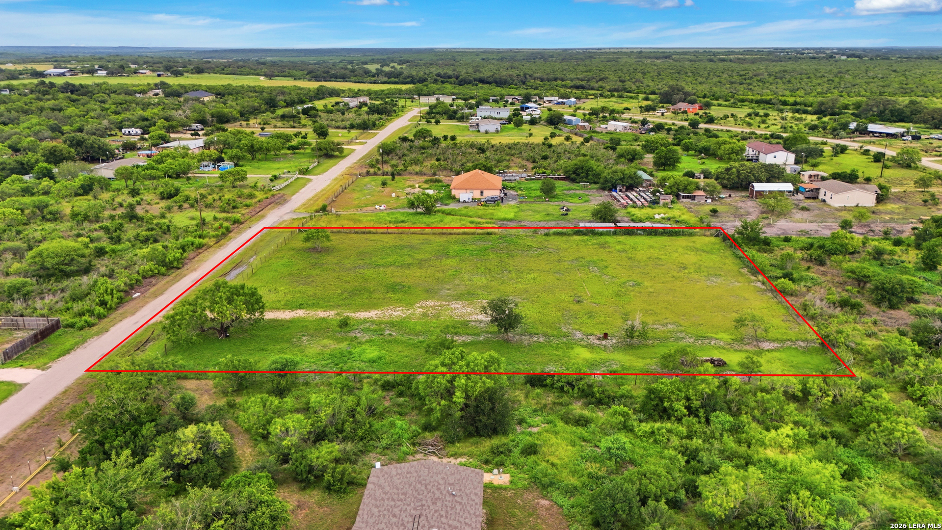 Aerial view of a grassy vacant parcel outlined in red, with a road along one side.