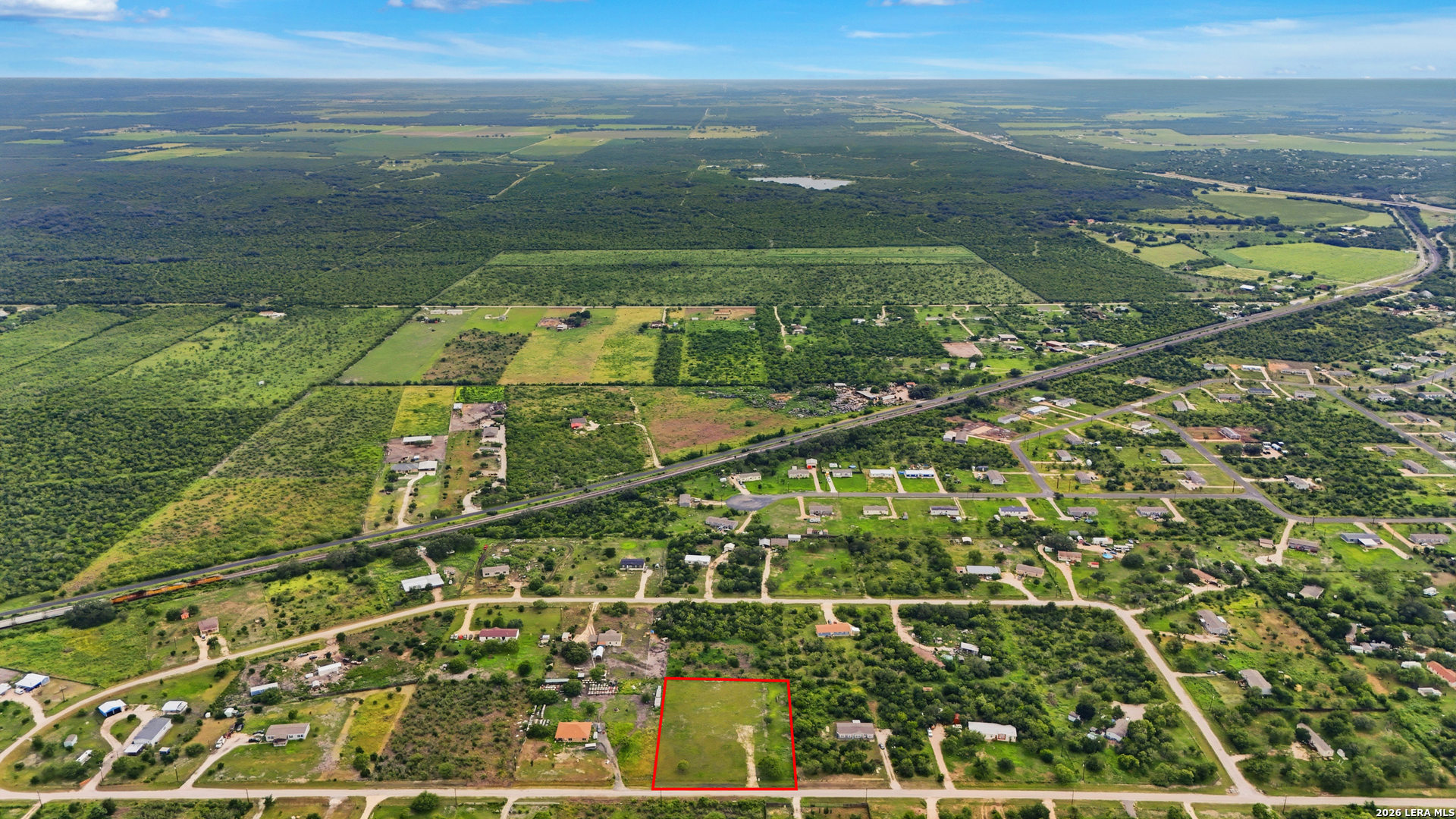 Aerial view of a grassy vacant lot outlined in red beside a residential road.