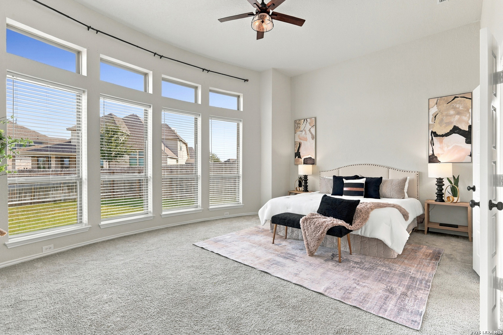 Staged bedroom with a bed, ceiling fan, and tall windows with blinds.