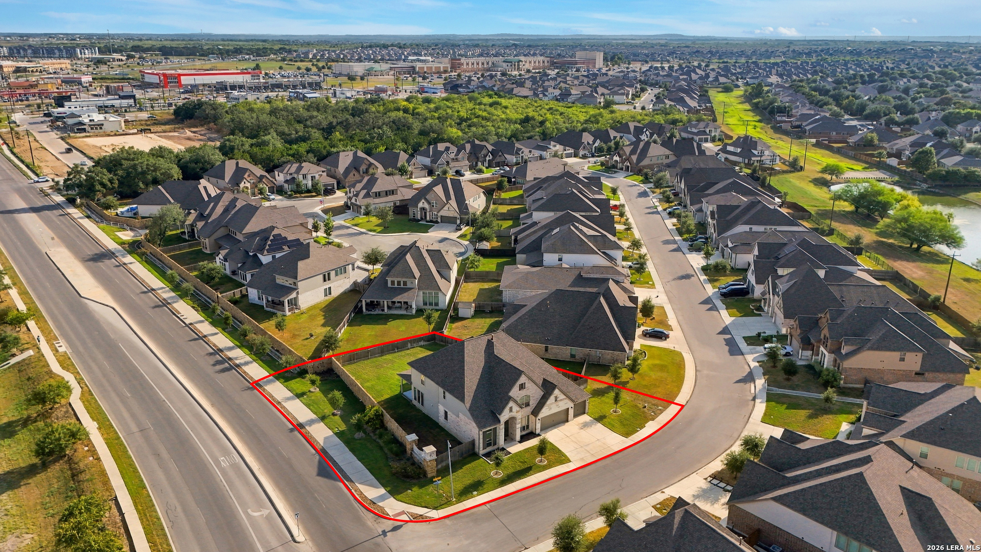 Aerial view of a corner-lot home outlined in red, with a fenced yard and suburban homes nearby.