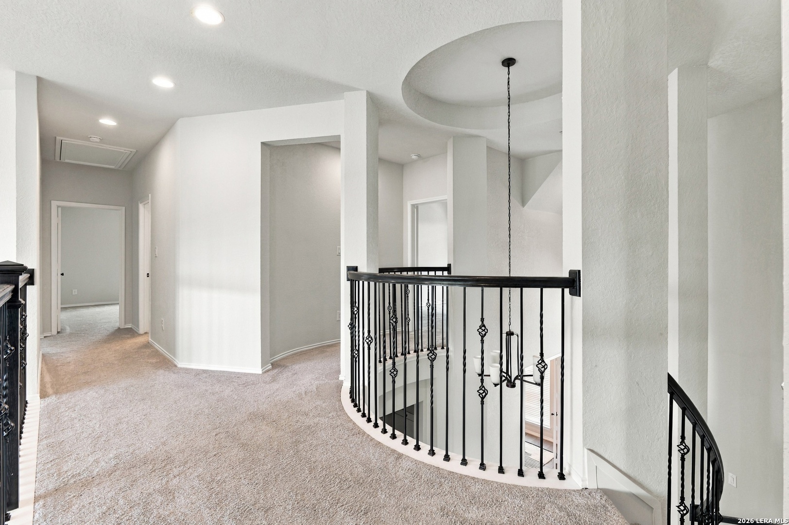 Carpeted upstairs landing overlooking an open staircase with ornate black railings and a hanging chandelier.