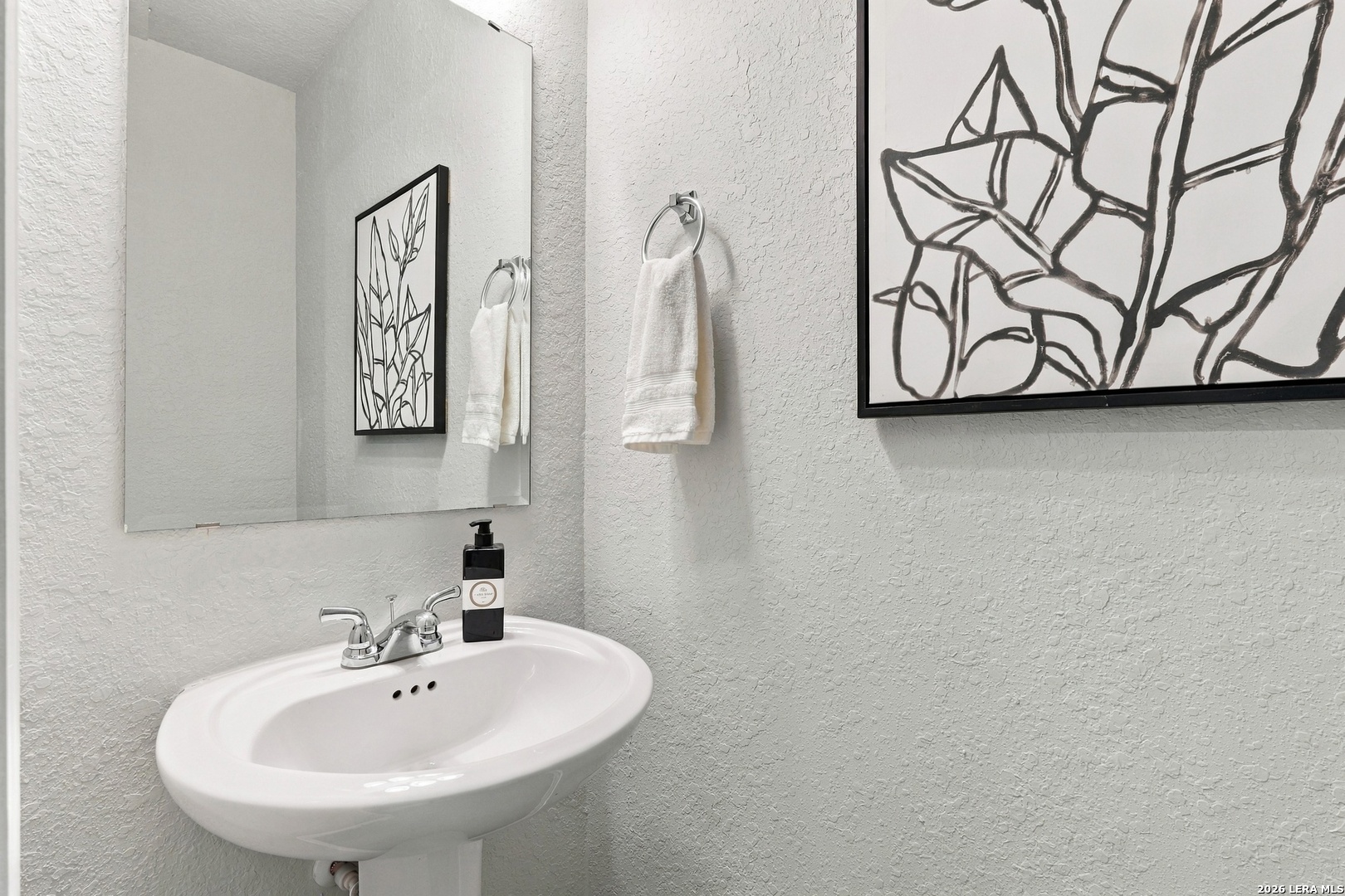 Bathroom sink with a chrome faucet, white towels, and black-and-white botanical artwork.