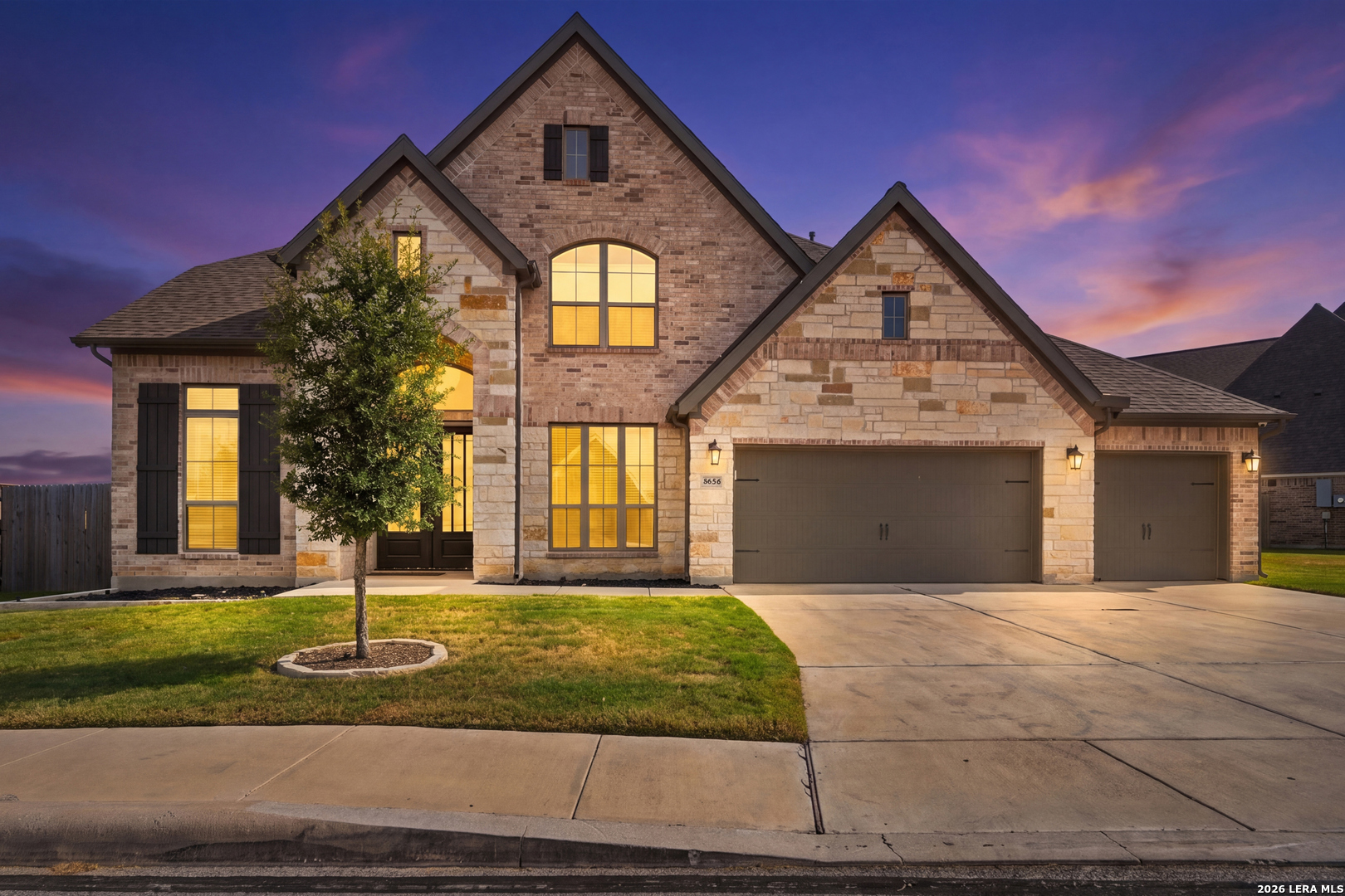 Two-story brick and stone home with illuminated windows and a three-car garage at dusk.