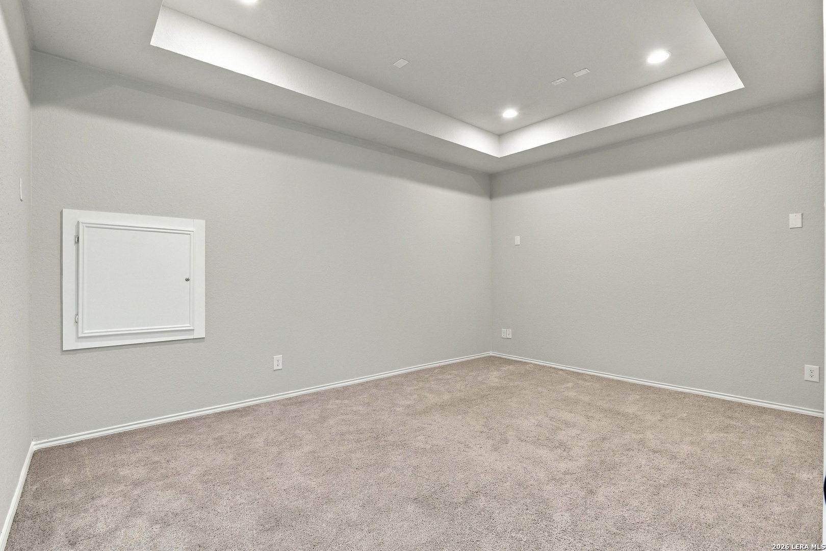 Empty carpeted room with a tray ceiling and wall access panel.