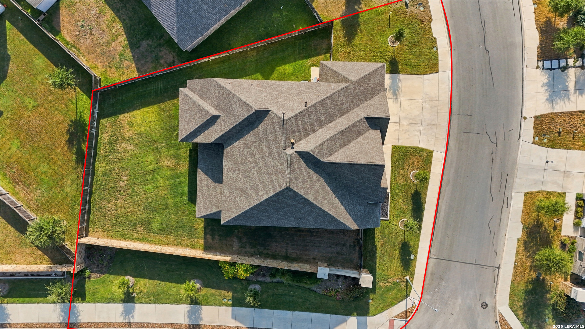 Aerial view of a house and fenced lot outlined in red beside the street.